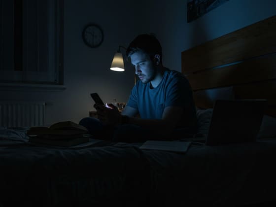 homem de 30 anos sentado na cama olhando para a tela do celular